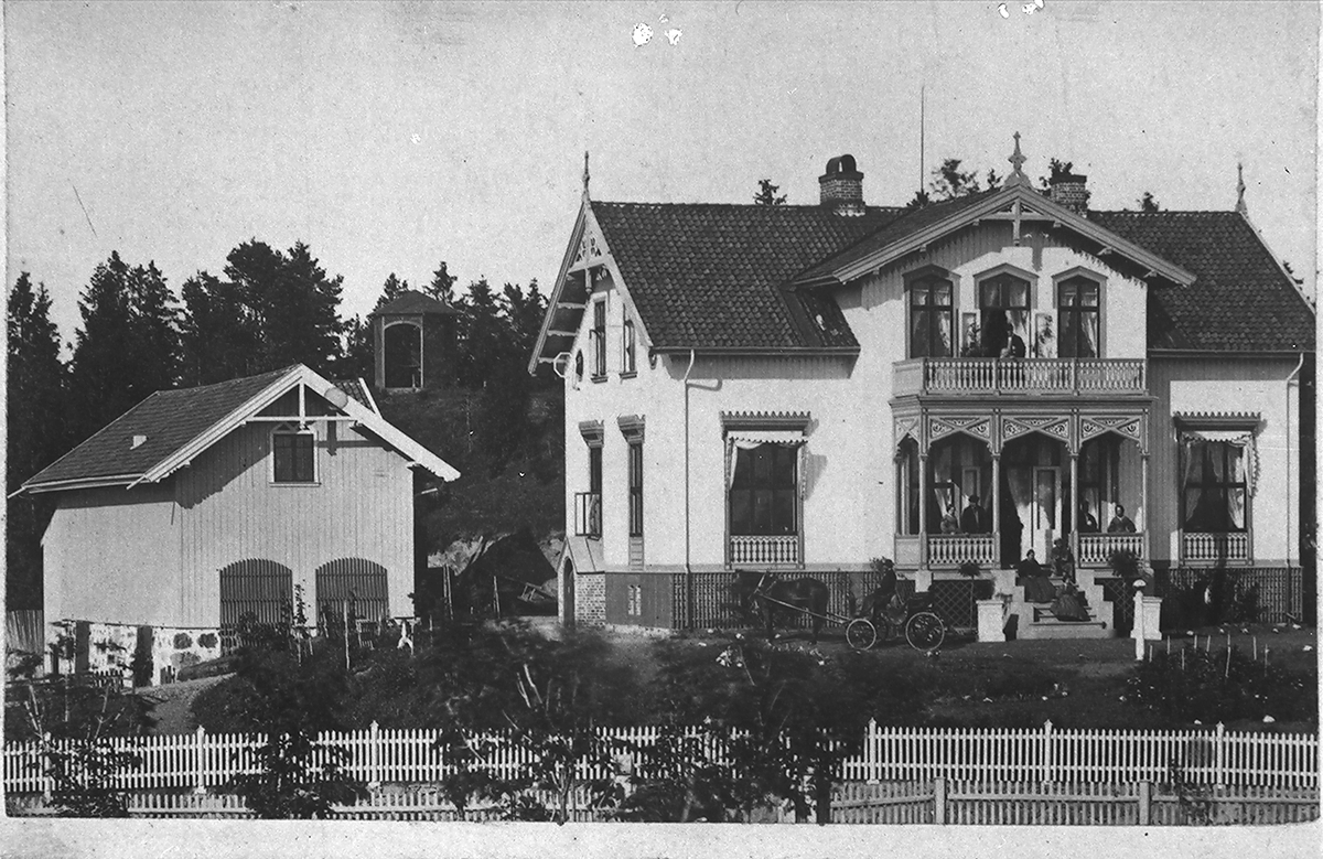Folk står på veranda i en villa, hest og kjerre i hagen. Fotografert 1924.