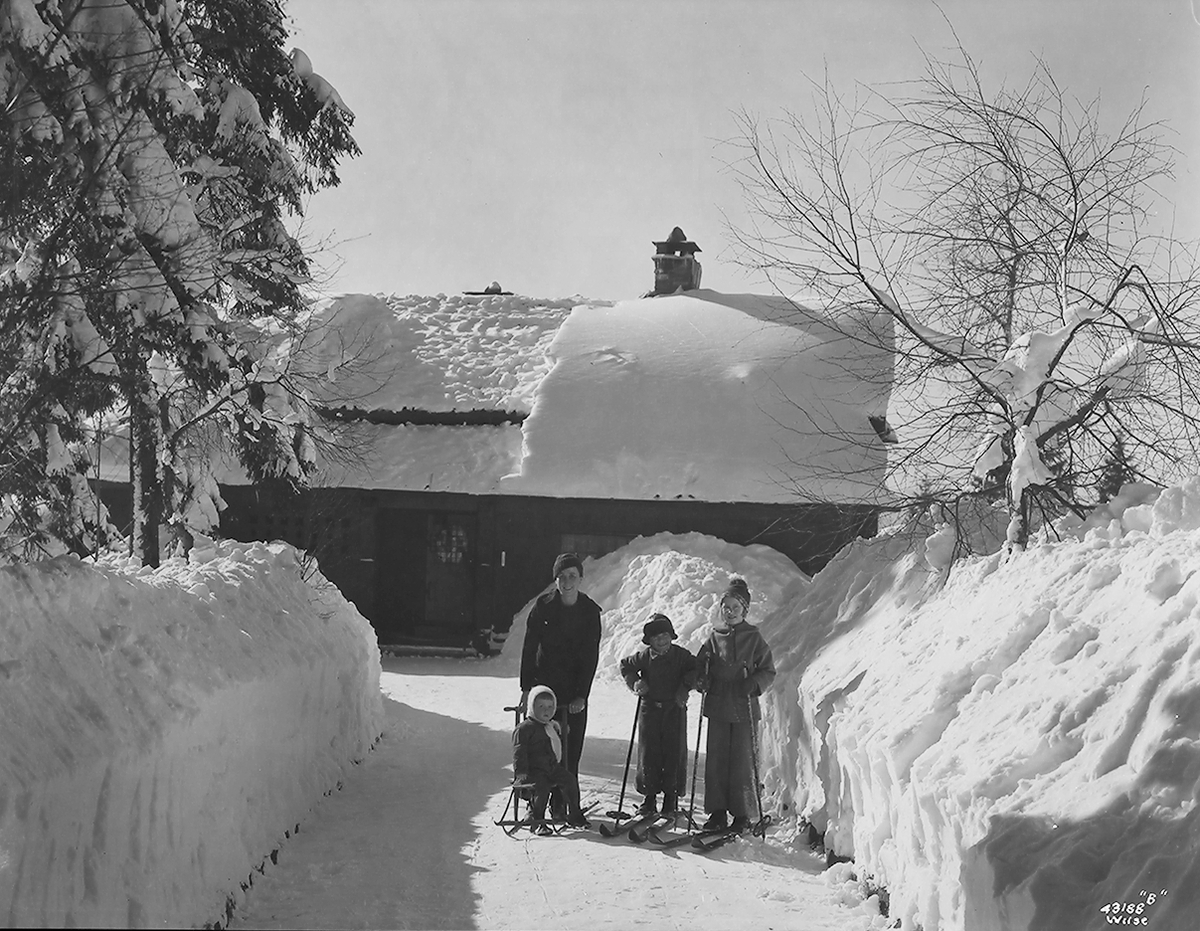 Kvinne og tre barn står foran et snødekket hus.