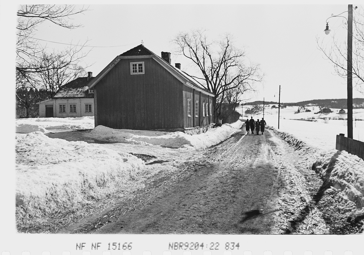 Personer ved eldre bygninger på vei i vårløsning. Fotografert 1941.