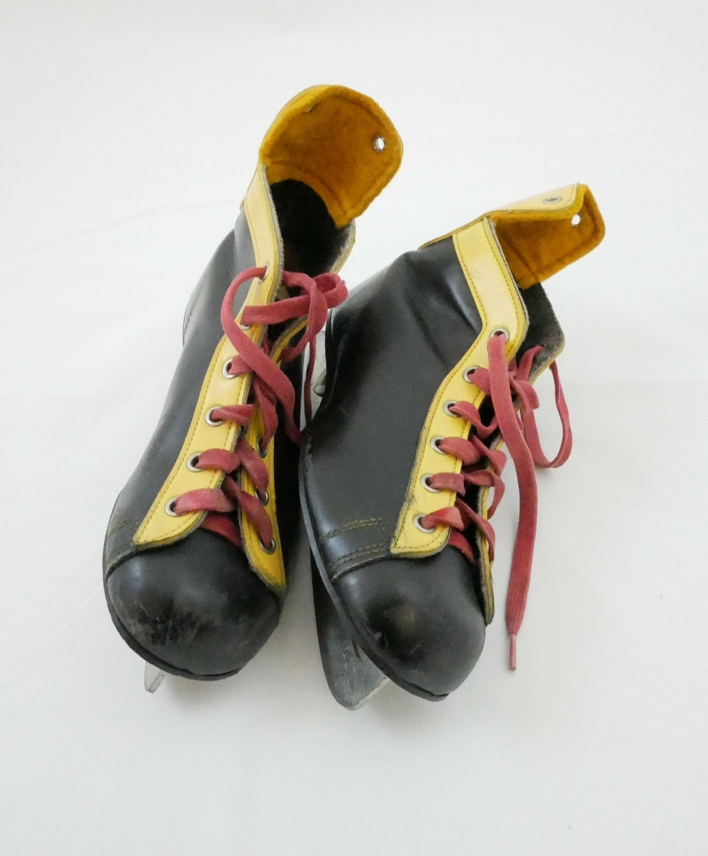 Skøyter med påfestede sko i sort og gult med røde lisser. Hvit såle på innsiden. 