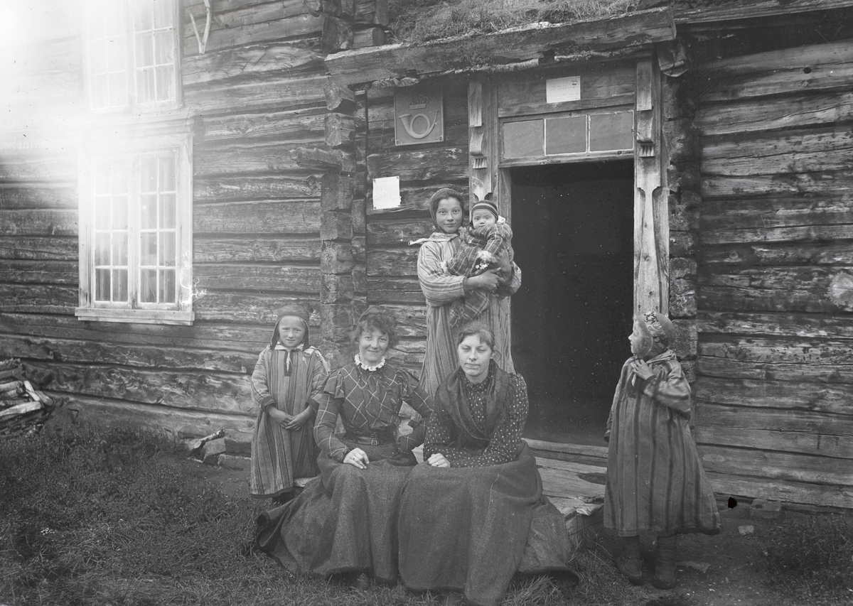 Gruppeportrett av noen kvinner og barn utenfor posthuset i Karasjok. Noen har samiske klær.