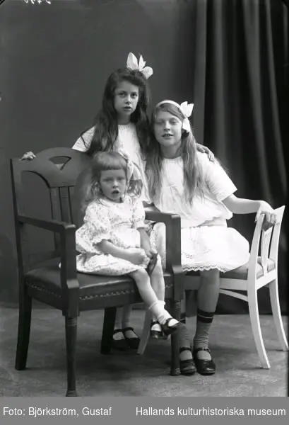Ateljéfoto med tre systrar där de två äldre har stora rosetter i håret. Beställare var doktorinnan Åberg.