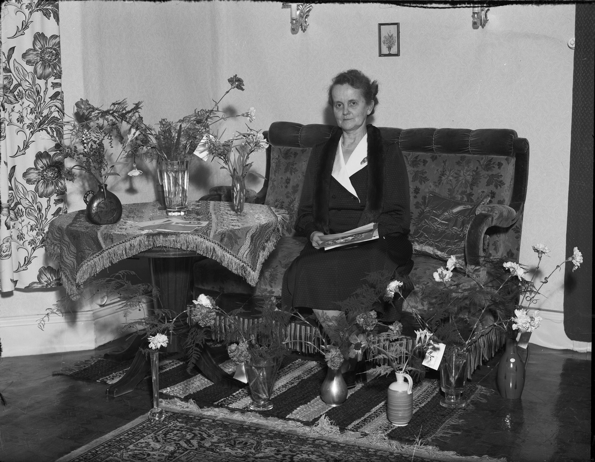 Kvinna i hemmiljö omgiven av blommor firar 60-årsdagen, Östhammar, Uppland