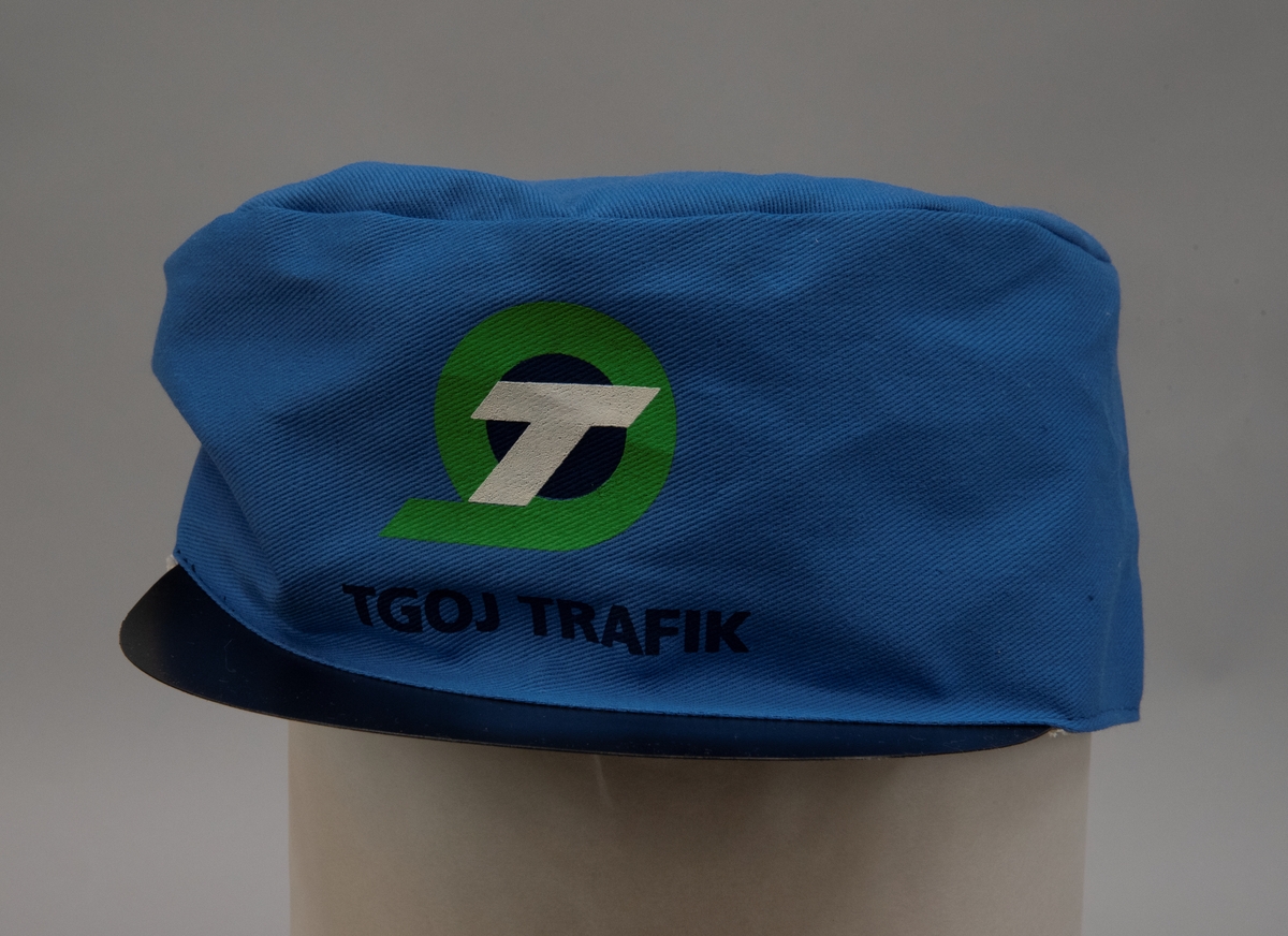 Ljusblå tygkeps med svart plastskärm och TGOJ Trafiks logotyp mitt fram. Resår baktill.