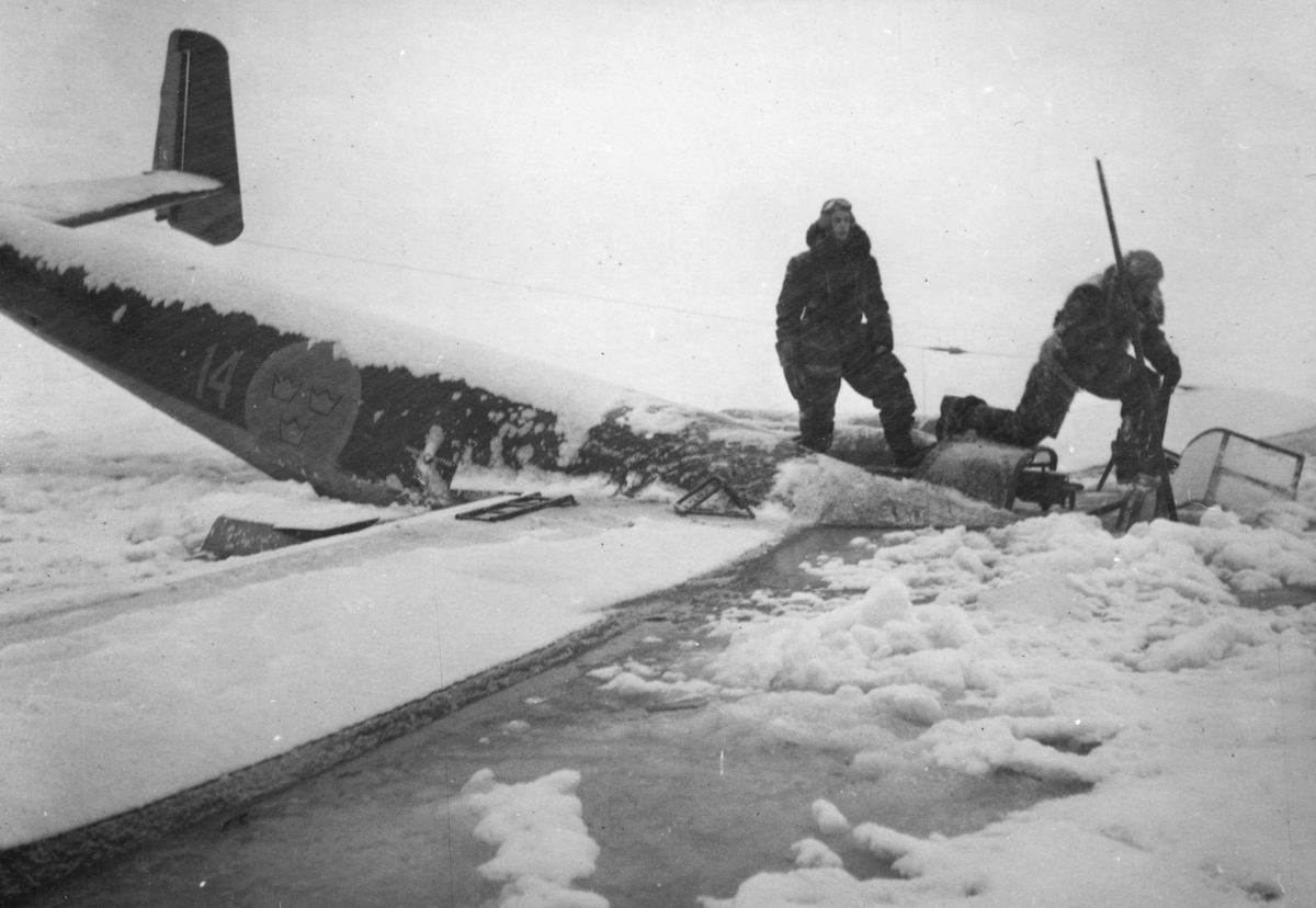 Flygplan B 18 Röd David ligger på isen utanför Härnösand efter nödlandning på isen den 10 februari 1946. Besättningen står på flygplanet.