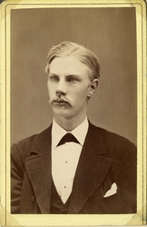 Porträttfoto av en ung man i kavajkostym med väst, stärkkrag