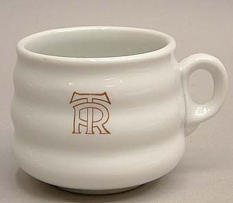 Kaffekopp av vitt porslin med två "midjor". Märkt i brunrött med logotyp för "TR"= Trafikrestauranger på sidan. Koppen kallas "Beckeböljakoppen" på grund av sin utformning.