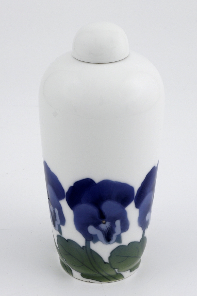 Vase i støpt porselen med tilhørende halvkuleformet lokk. Nedre del av korpus er dekorert med en bord av stemorsblomster i underglasurmaling. Liten sirkulær munning.
