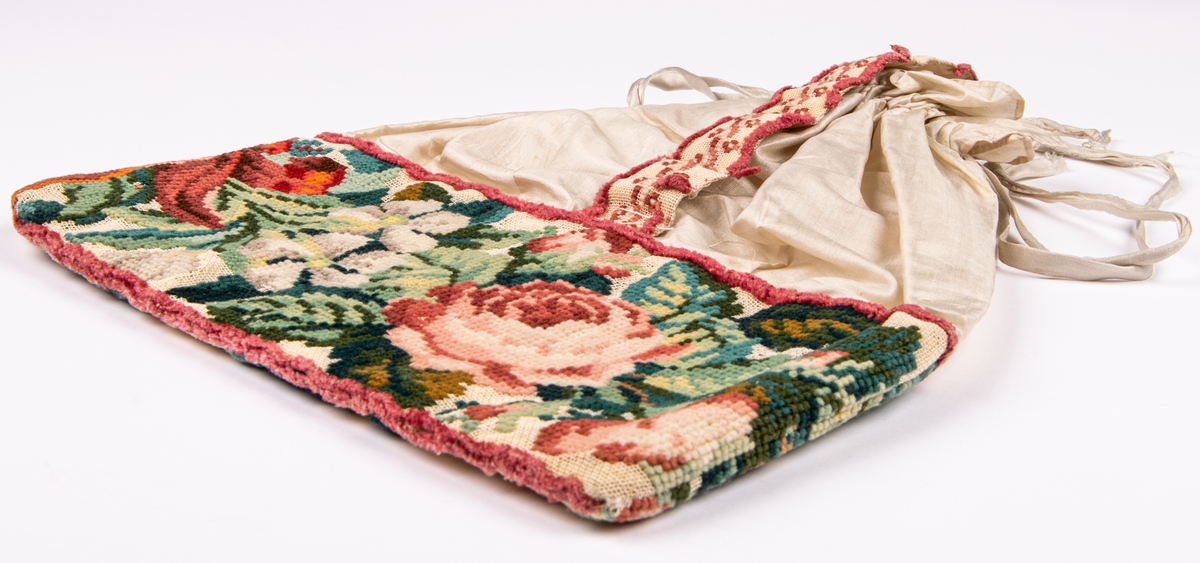 Väska i siden med broderad bård på stramalj, rosor i olika färger. 
Påsmodell, band att dra ihop och bära med.