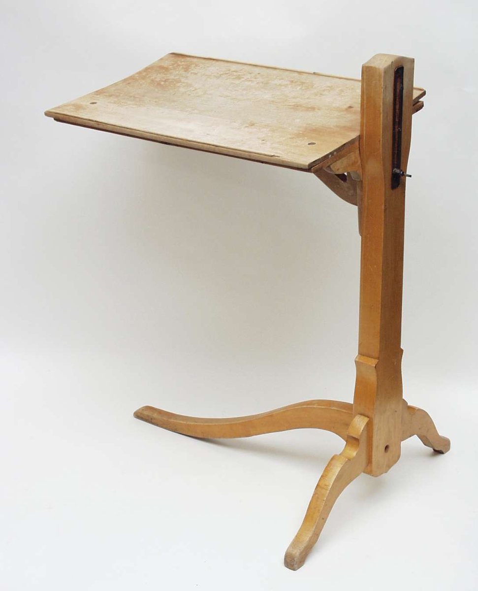 Bordet har plate med opphøyde kanter og stolpe med høydeskyver. Bordet har tre ben, to korte og ett lengre som følger bordlengden.
