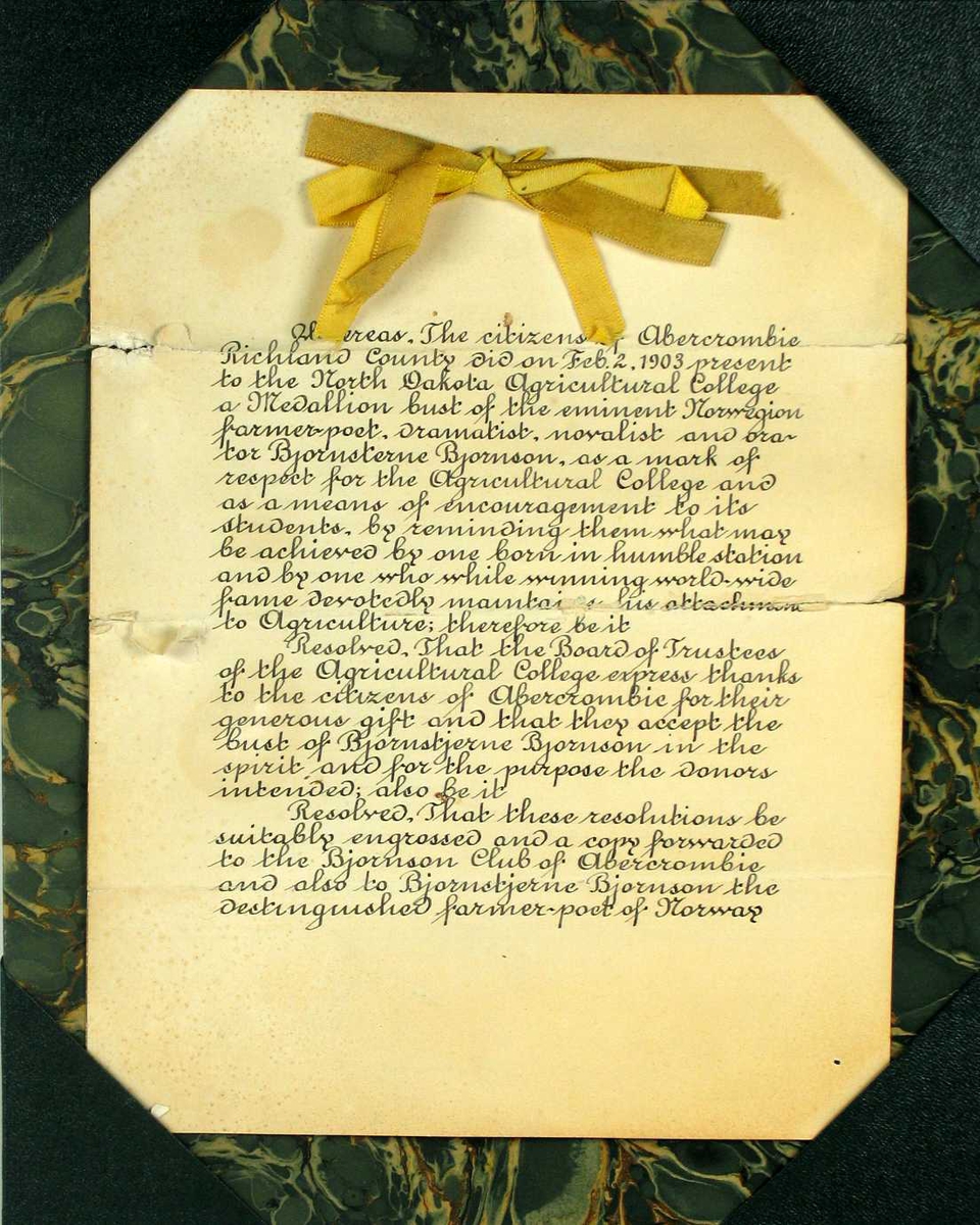 Brev med grønn marmorert pappstøtte. Brevet er håndskrevet og har en gyllen silkesløyfe øverst.