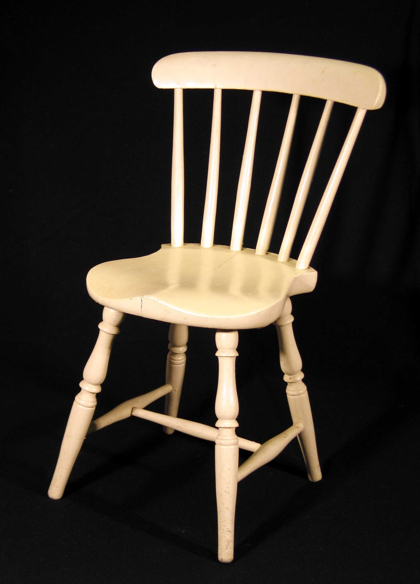 Hvitmalt pinnestol for barn. Den har dreide profilerte bein, sprosser og staver i ryggen.