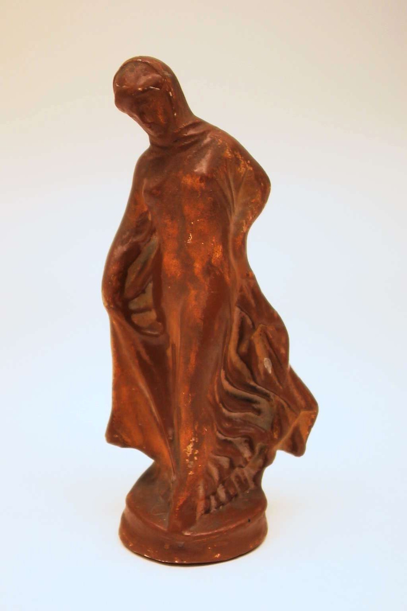 En stående kvinnefigur støpt i gips. Figuren er malt brun.