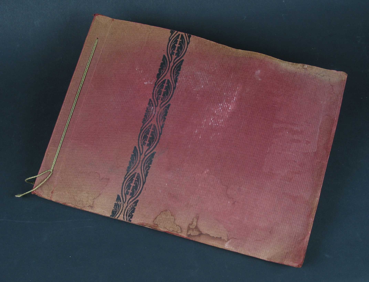 Fotoalbum i rød kartong med svart mønsterbord på omslaget. Sidene er av gråbrun kartong. I ryggen er det en grønn tvinnet snor.