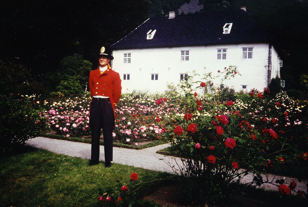 uniformer, mann i gammel dansk postuniform utenfor Rosendal Baroni, roser i bedene