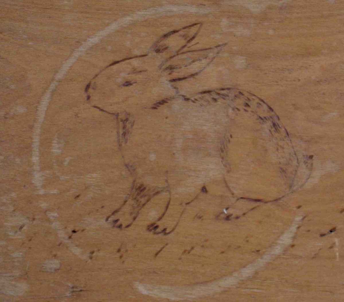 Bilde av en kanin, svidd inn i bunnen av trauet. Enkelt vegetabilsk motiv på handtakene i trauets kortsider.
