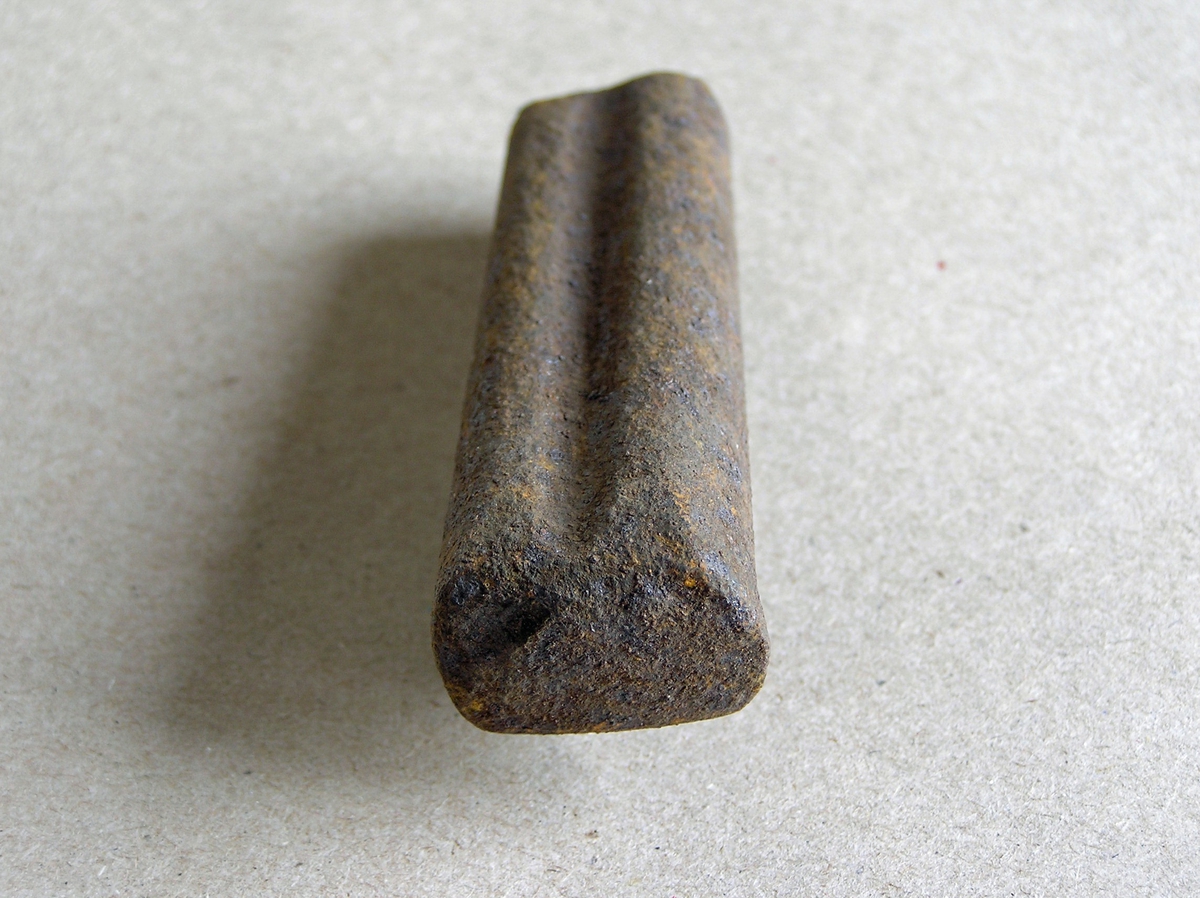 Smidd jernstykke til bruk ved smiing av merkeøks. Merket ble formet rundt stempelet. Uten håndtak - antagelig holdt med tang. Noe rust.