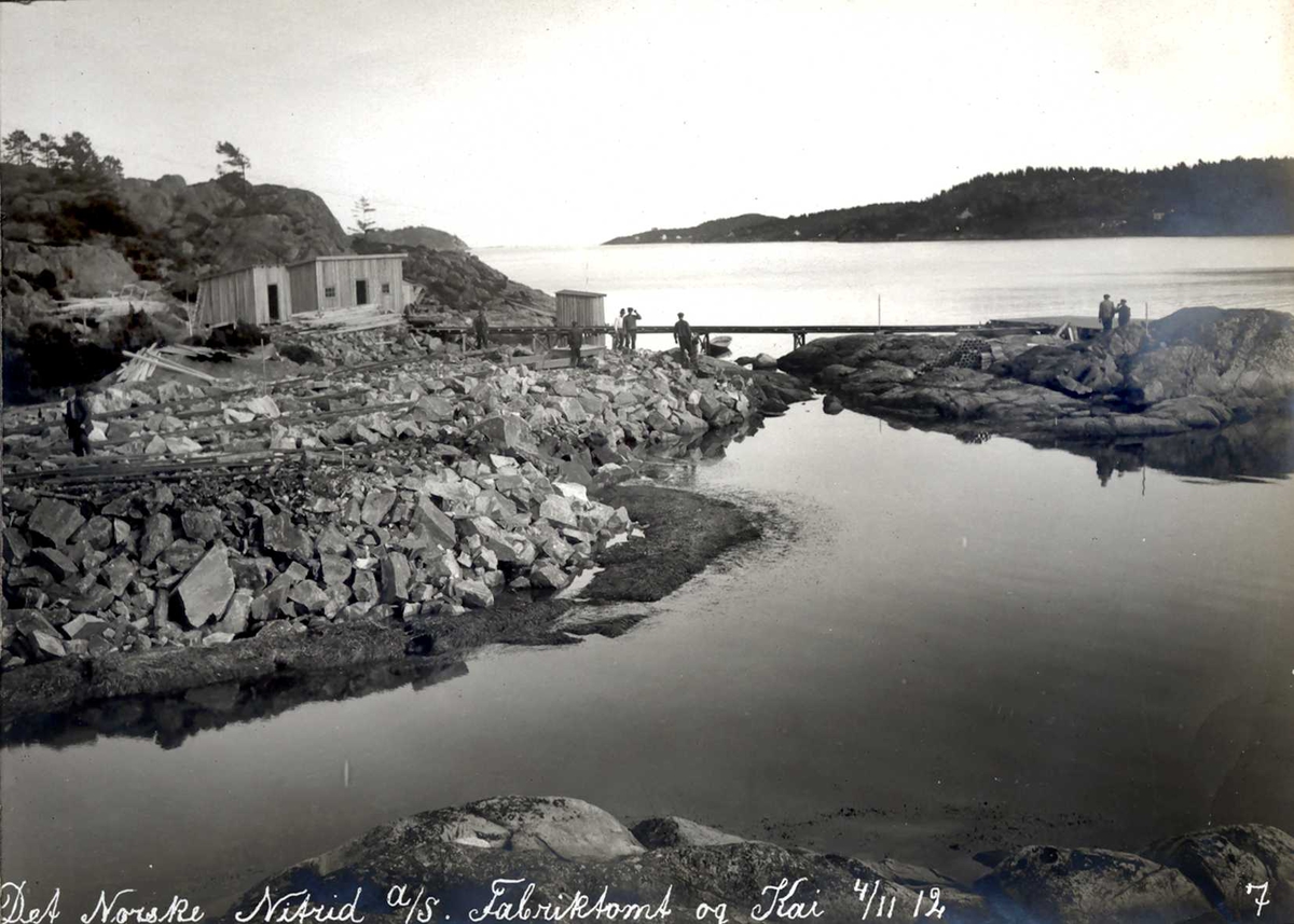 "04/11-1912" Nitriden. Utsprengte masser fra tomtearbeidene fylles i sjøen og ut til et skjær. Anleggsbrakker. Tromøysund og Tromøy til høyre.