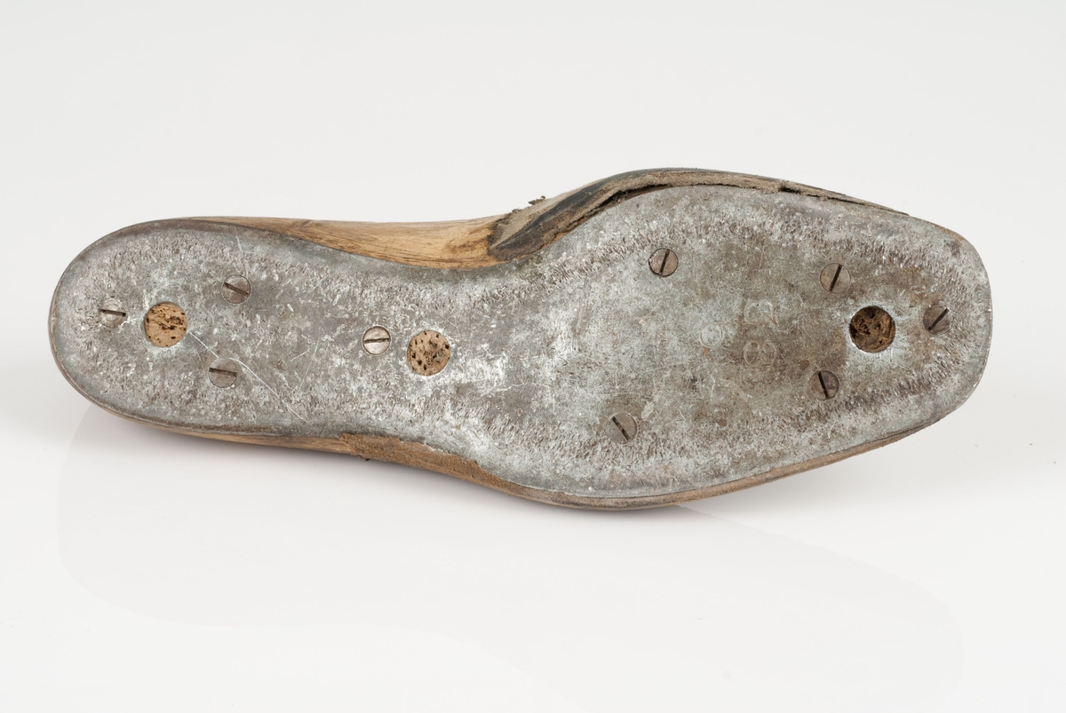 En tremodell i to deler; lest og opplest/overlest (kile).
Venstrefot i skostørrelse 38, og 6 cm i vidde.
Såle av metall.
