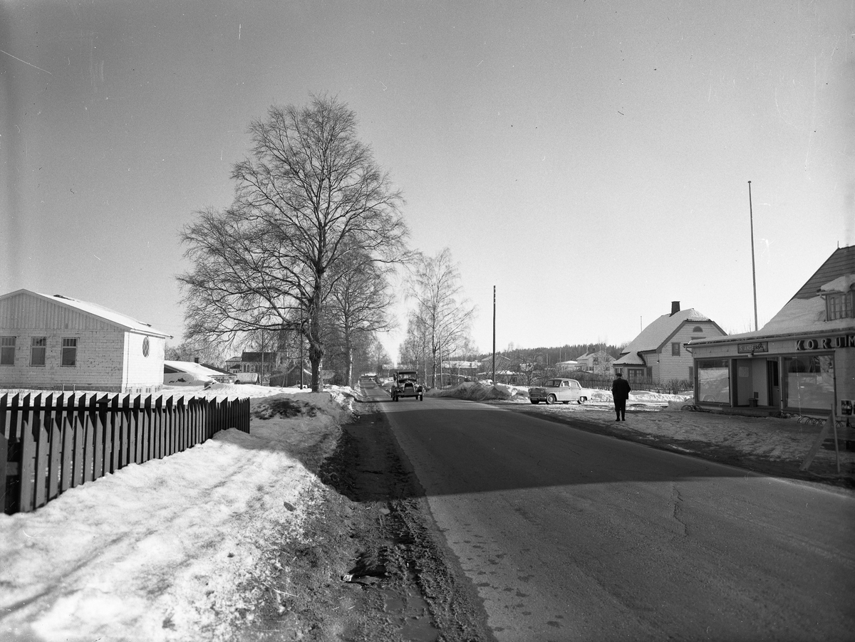 Råholt. Før- og etterkrigs biler. S Andersson KORUM.. står på forretningen til høyre. Menighetshuset til venstre. Kirken i bakgrunnen.
