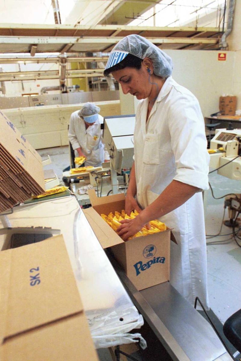 Pepitakjeks legges i kartong, emballasje, arbeidere, kvinner, arbeidstøy, arbeidsmiljø, fabrikkmiljø, maskiner
