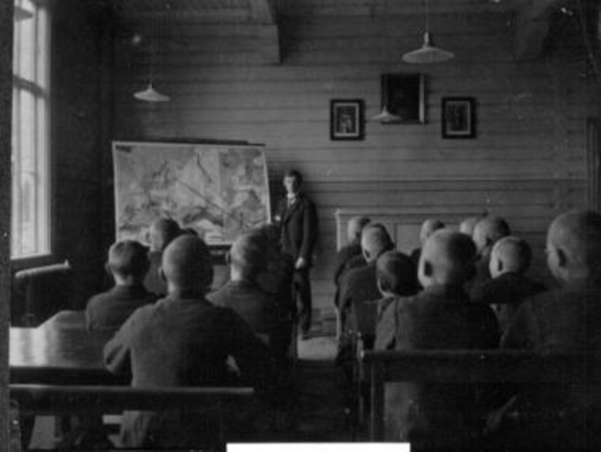 Interiør fra klasserom på Toftes Gave, Nedre Sund, Helgøya. Lærer underviser elever i geografi med kart.