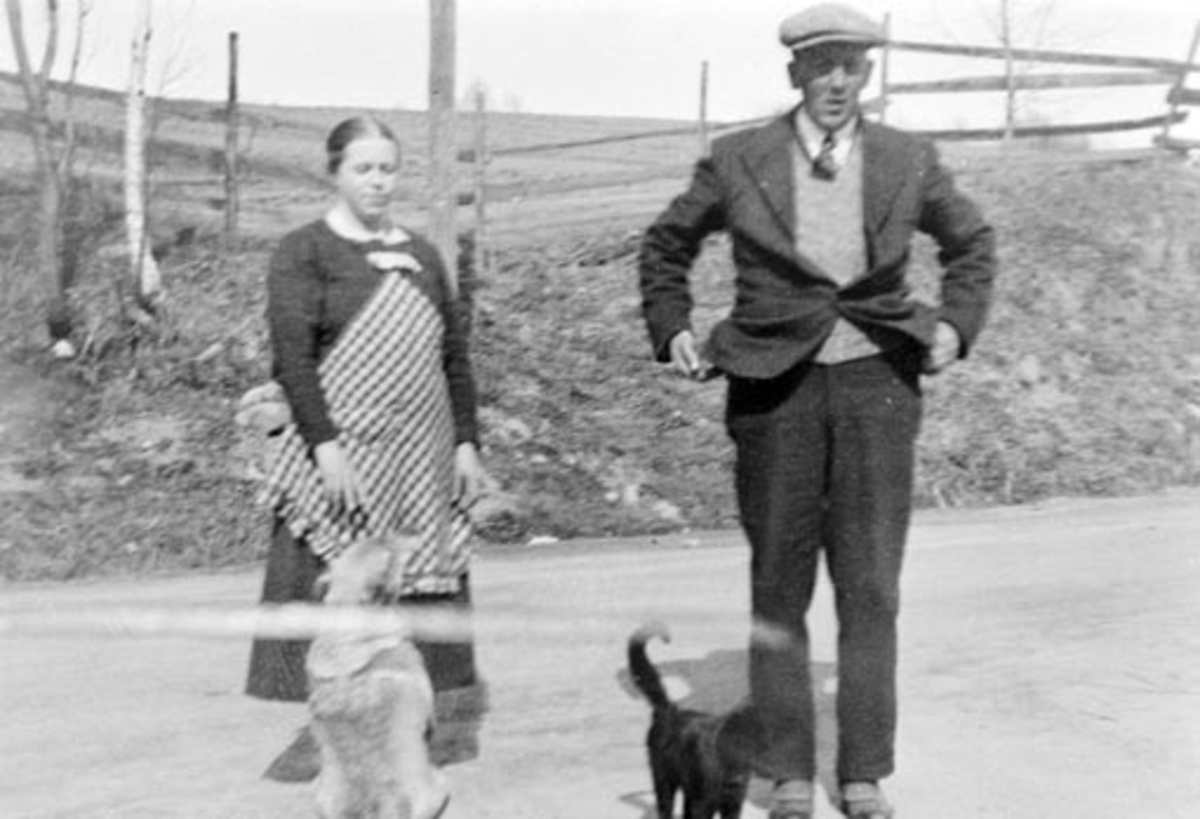Husholderske og butikkdame Tora Johansen med hund og ekspeditør Jens Evensen Mengshoel (1897-1971) med katt i vegen utenfor landhandleriet Svingen på Mengshoel fergested.