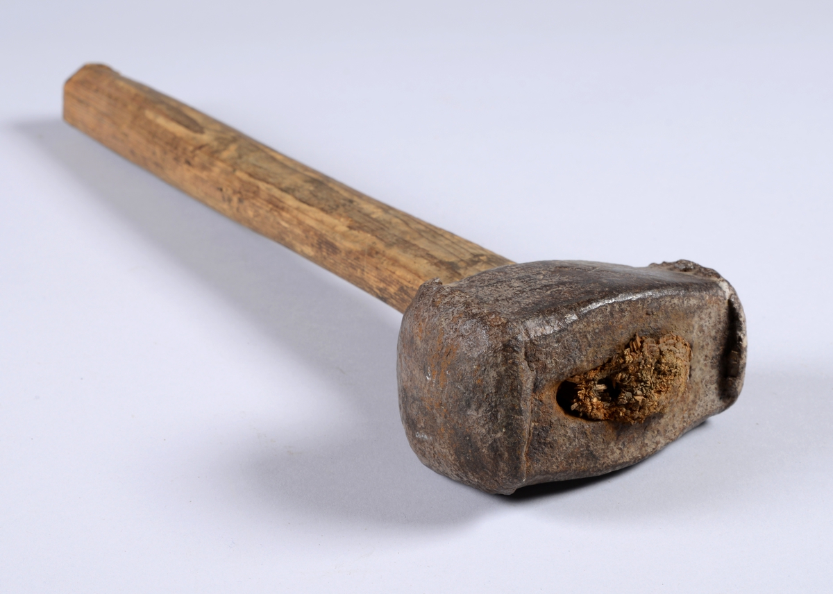 Hammer med ovalt strakt skaft. Skaftet er noe flatere ved hammeren. Hammeren har et innstøpt merke, et kryss, på ene langsiden. Den er brukt på begge ender. På grunn av slagene mot hardt berg har hammeren fått skjegg.