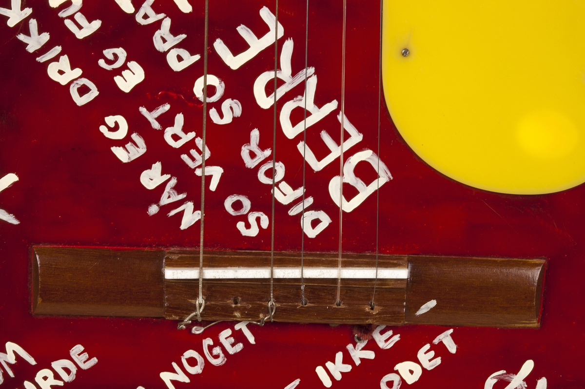 Akustisk gitar med rødmalt lokk med påført hvit skrift og gult plekterbrett. På gitarkroppens sider, hals og hode sees originallakk i sunburst. Fingerbrett i mørkt tre og sal i ben.