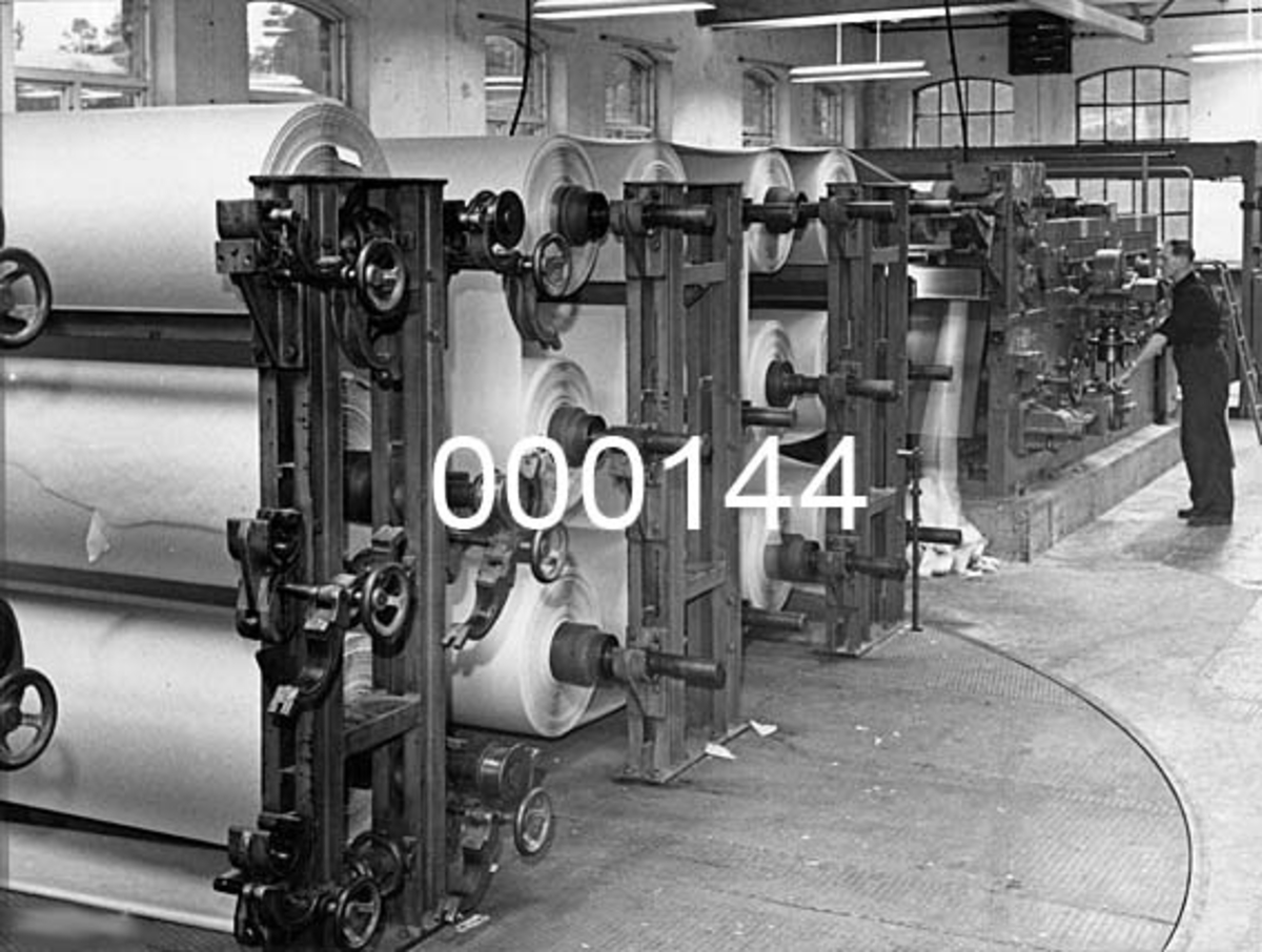 Interiør fra Drammenselvens Papirfabrikker på Geithus i Modum kommune i Buskerud.  Fotografiet viser skjæremaskinen, som her betjenes av Kristian Borgen (1900-2003). 