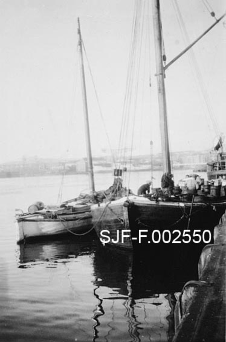Båter, fotografert ved kaia til Schwencke & Co's Eftf., antakelig ved Kongshavn, der firmaet framstilte tjærebaserte produkter fram til 1924.  Nærmest kaia (til høyre) ser vi baugenden på en forholdsvis bred, kraftig lastebåt med treskrog.  Utenfor (til venstre) ligger en mindre, kvitmalt seilbåt, mer en lystbåttype.  Ifølge en innskrift i albumet fotografiet er hentet fra skal båtene ha hatt navnene "Måken" og "Anna".  I bakgrunnen skimtes en del bymessig bebyggelse, antakelig i Oslo havn. 
