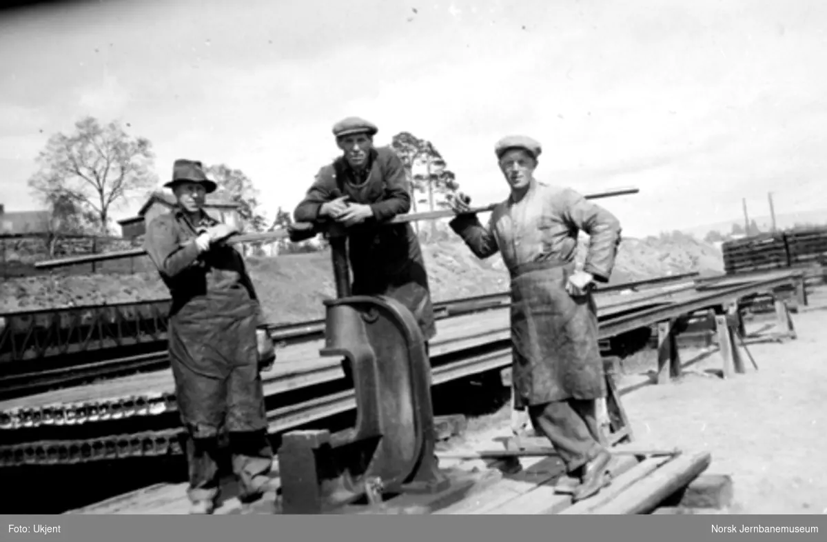 Tre banearbeidere ved en skinnepresse