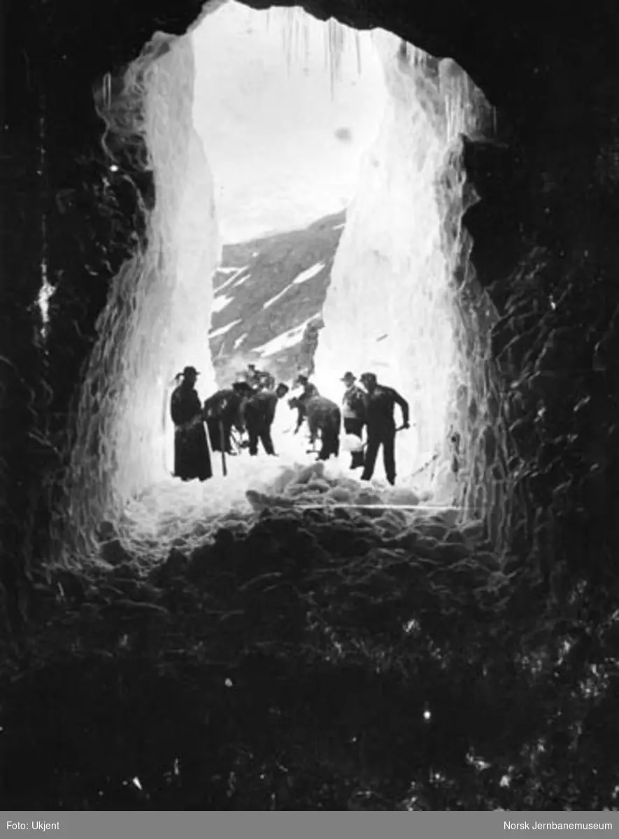 En gjeng snømåkere ved inngangen til en tunnel med et damplok i bakgrunnen