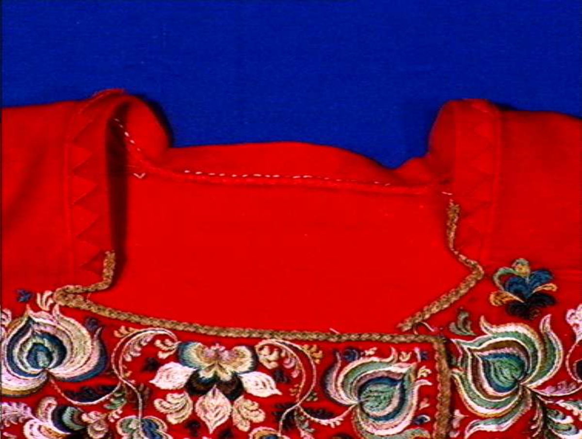 Rød trøye i klede med brodert dekor i silke, mørkrød kant ned.