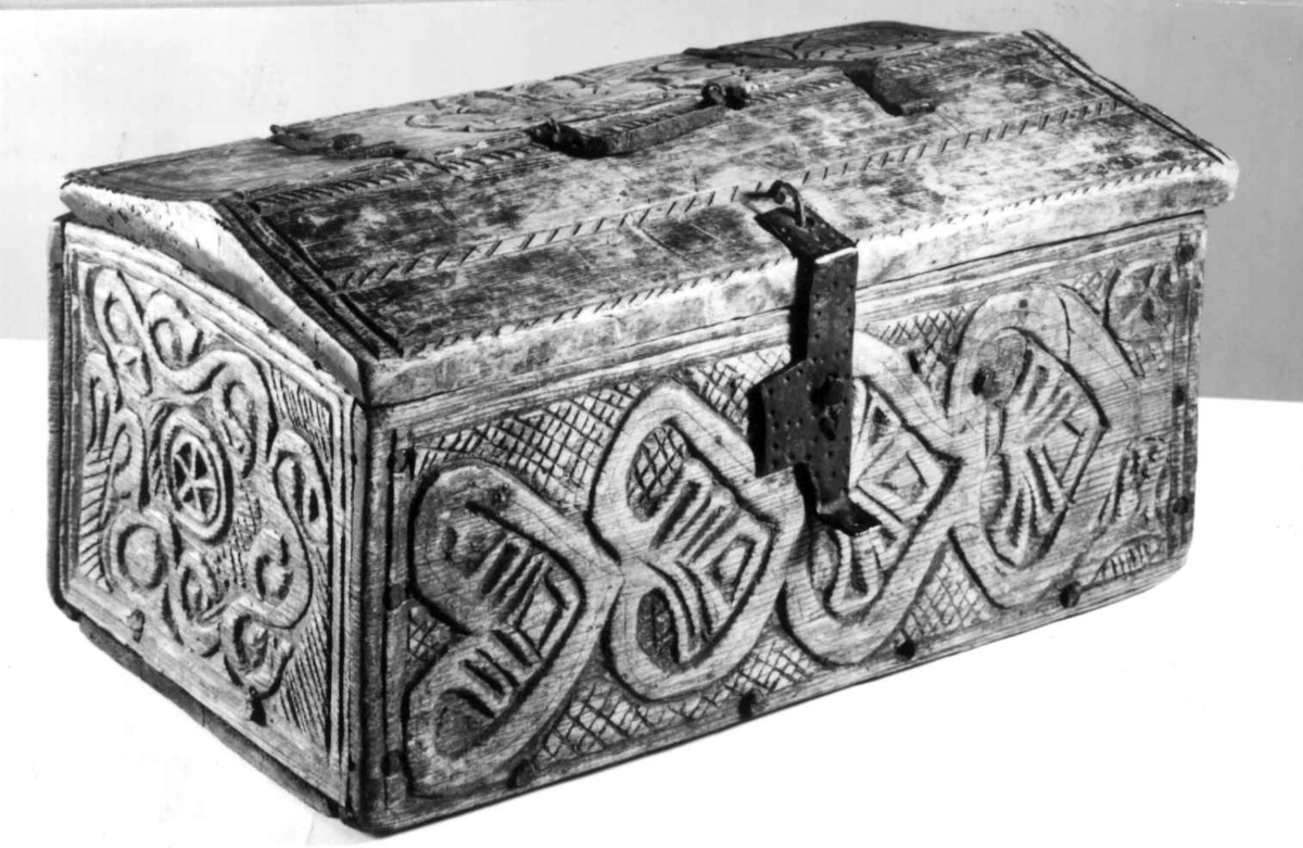 Skrin med flate sider of lett takformet lokk. Hengslet i bakkant og låsmekanisme i forkant. Håndtak midt på lokket. Hele utsidenhar skurd dekor med ranker, dyr og mennesker.