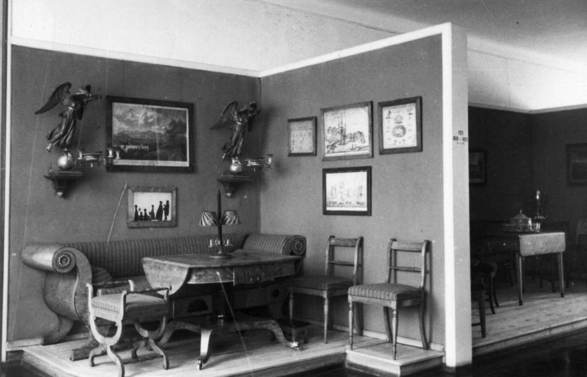 Interiør i empirestil som utstilt i Bysamlingen på Norsk Folkemuseum. Motivet viser et lite, møblert rom med landskapsmalerier og silhuetter på veggene.