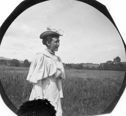 Frk. Solveig Berg i landskap med åker/eng og skogholt.