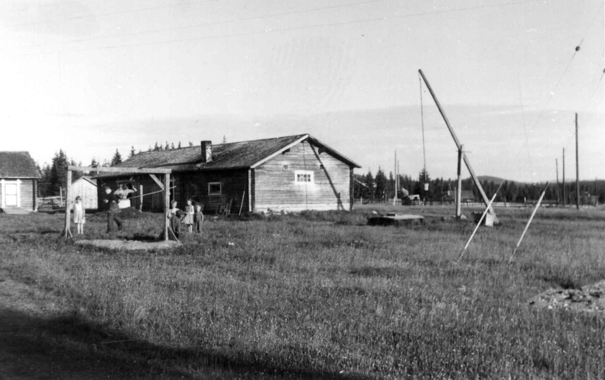 En fjøsbygning med brønn i forgrunnen, og barn som leker. Aapua 1958.