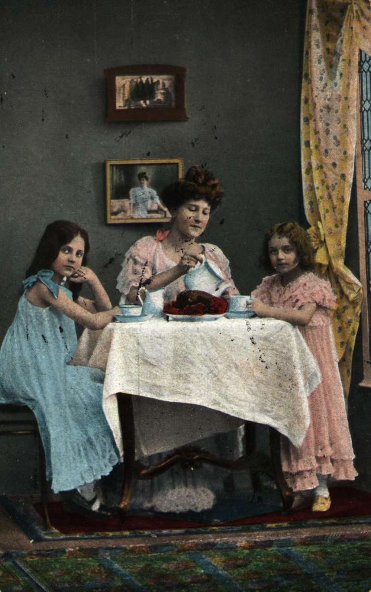Postkort. Jule- og nyttårshilsen. Fargefoto. Interiør stue. Mor og to barn sitter til bords.. Stemplet 21.12.1903