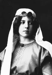 Studioportrett av kvinne i kostyme med slør og smykke rundt 