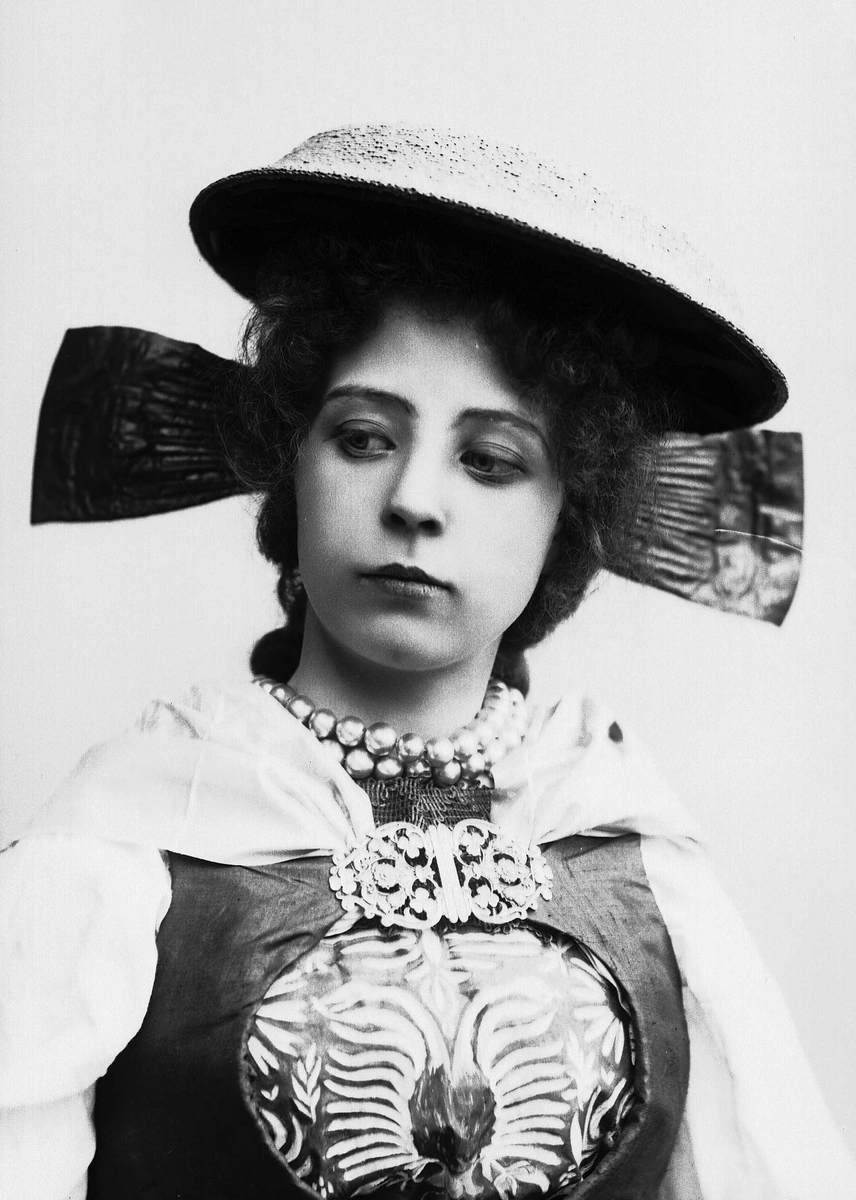 Brystportrett av kvinne i drakt og hatt, med perlekjede i halsen.