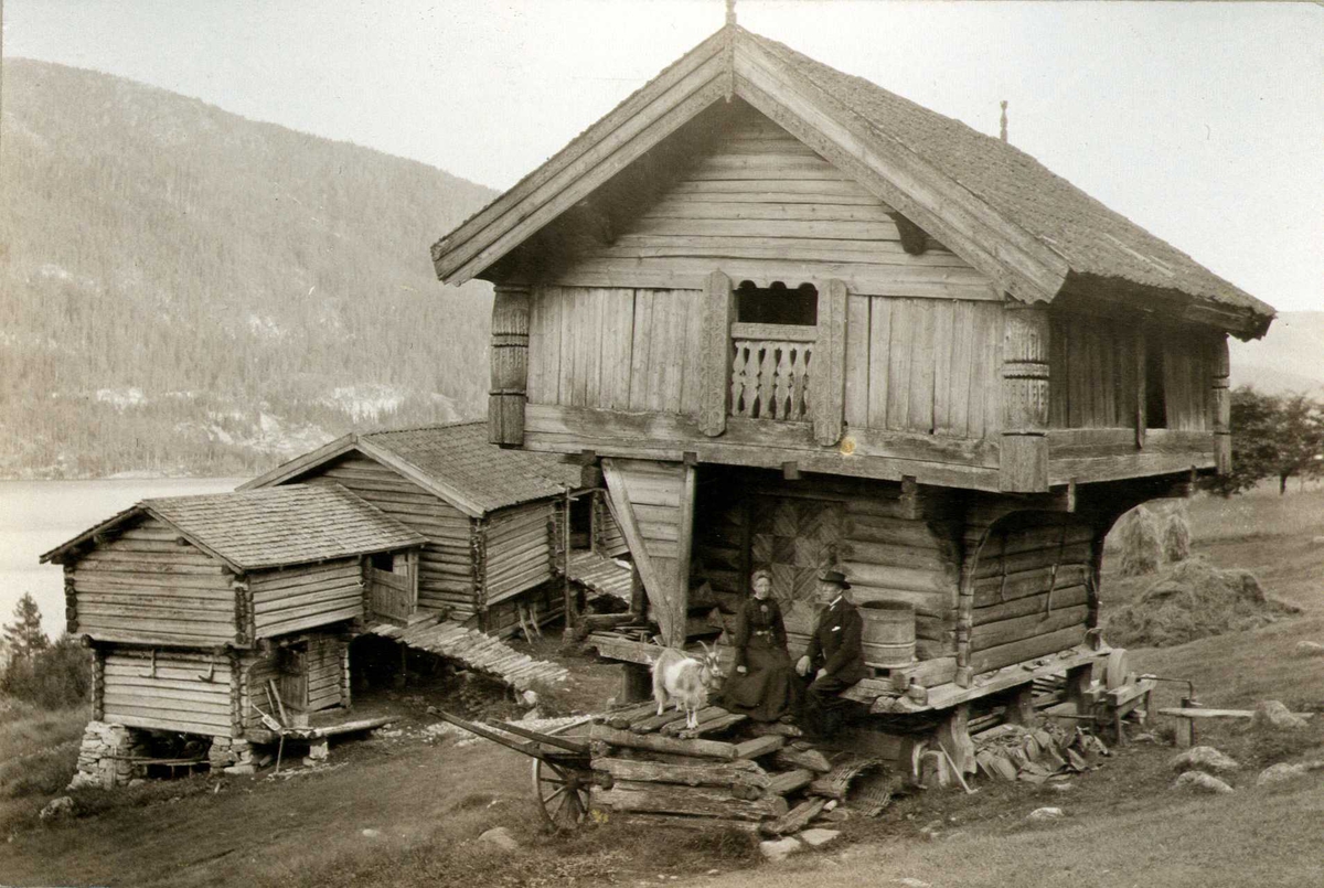 Del av gårdstun, Lynnevik, Gransherad, Notodden, Telemark. Mann og kvinne sittende foran loftet. Fotografert 1907. 