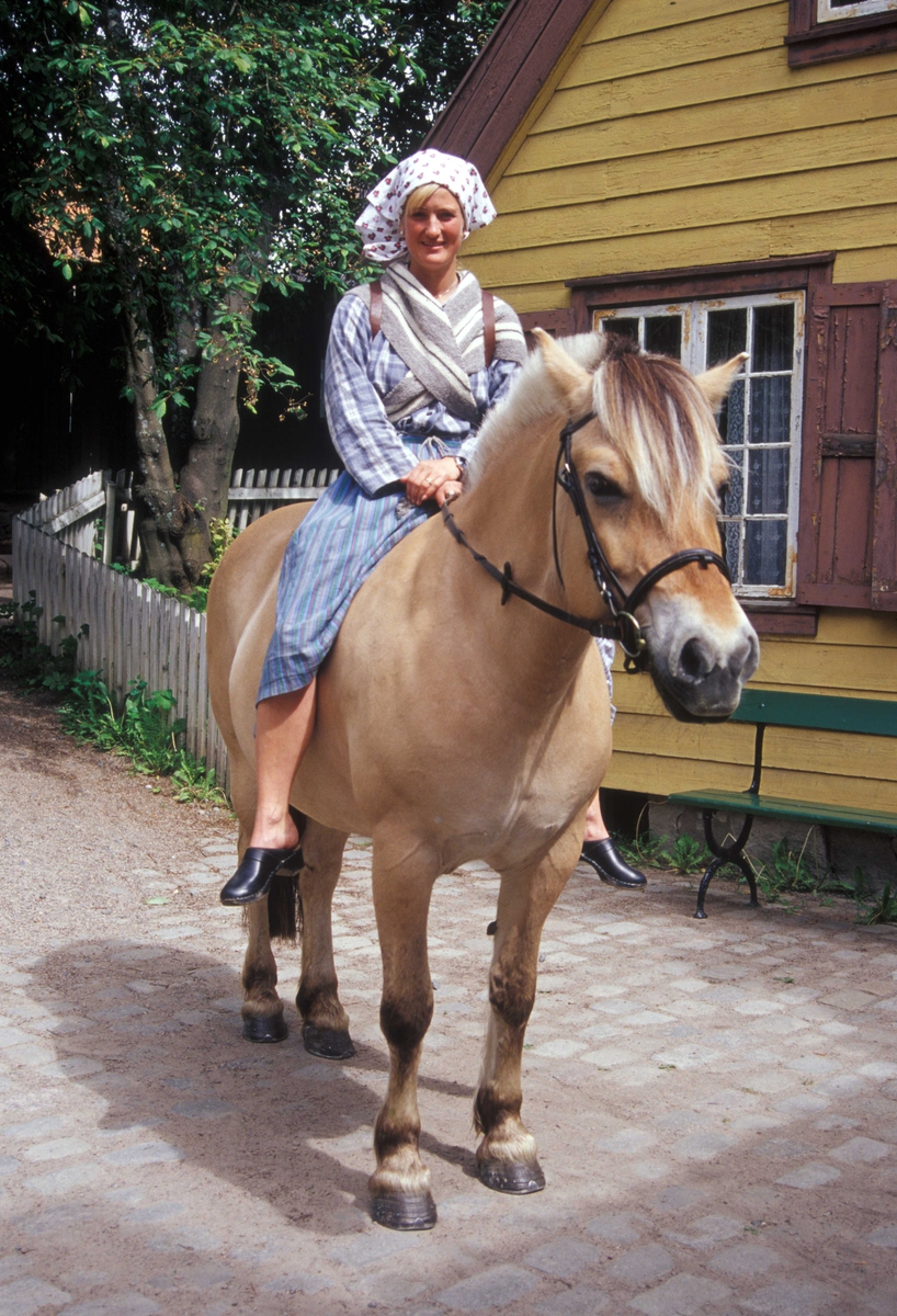 Kvinne i drakt ridende på hesten Tordis på Enerhaugen, Norsk Folkemuseum.