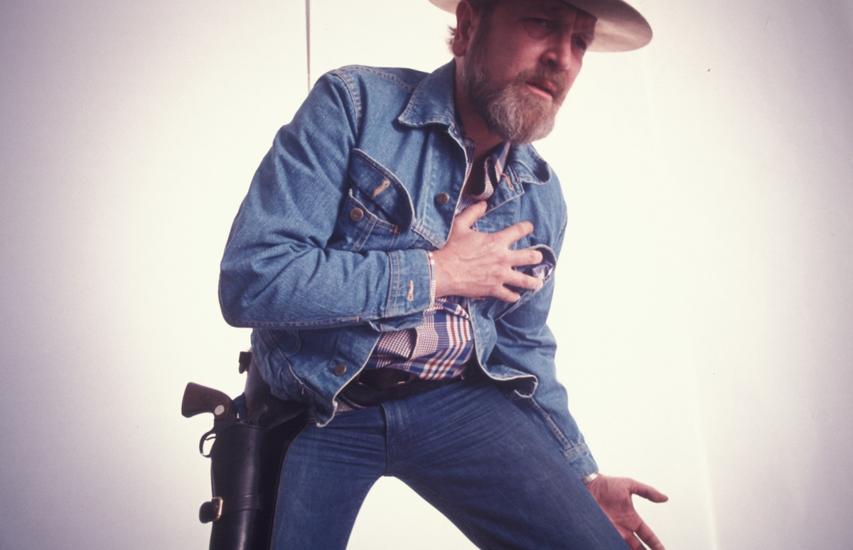 Reklamefoto. Mann ikledd cowboykostyme blir truffet av skudd fra revolver. Kampanje for tobakksmerket Petterøes Veteran 1975.