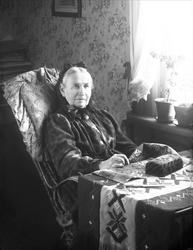 Portrett, eldre kvinne i svart, sittende med håndarbeid. Fru