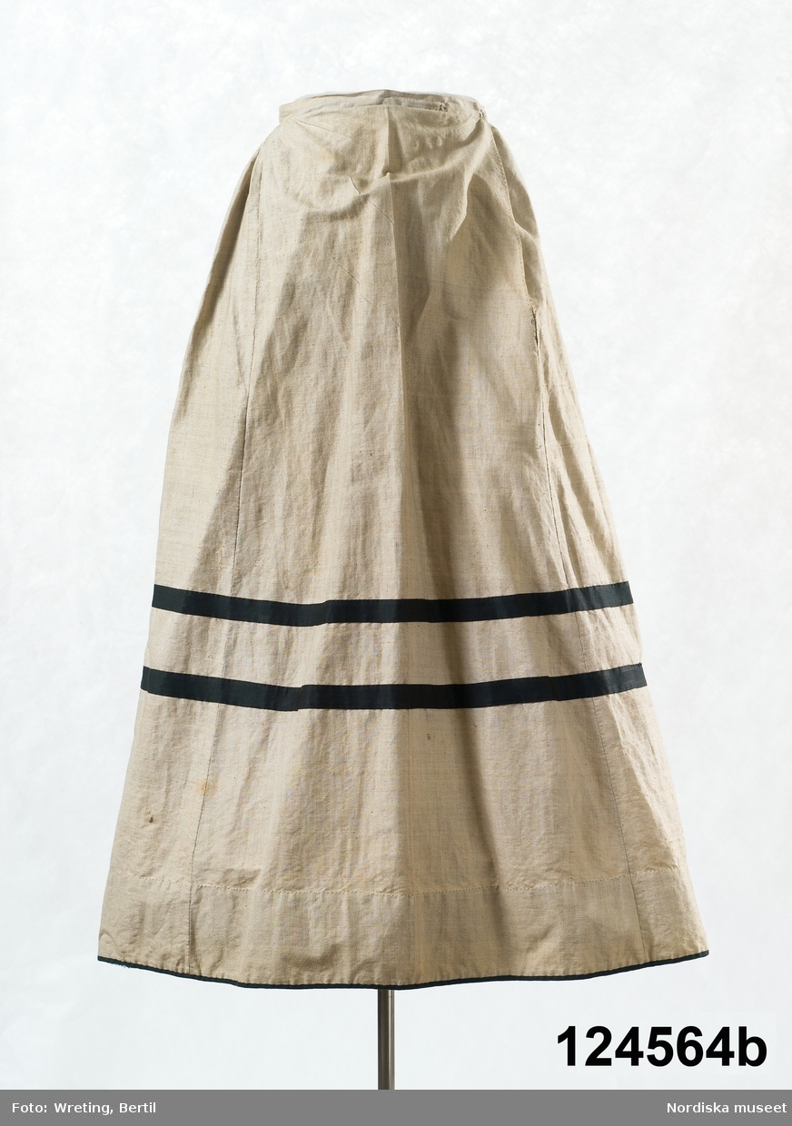 2-delad klänning i  modesnitt från 1870-talet. Med liv och kjol av oblekt fintrådig bomullslärft. varpen vanlig bomullstråd medan inslage tär en glansigare tråd. Handvävt med små vävfel. 
a. Livet, höftlångt, figursytt. 2 framstycken, släta och något utställda nedtill i sidsömmarna. Nederkanten något svängd. 4 ryggstycken insvängda i midjan för att sedan vidgas i ett rundat skört. Nederkanten kantad med 2 cm brett svart bomullssatinband. Isydd ärm med 2 sömmar. Tät halsringning med låg ståndkrage. Knäpps med 7 blanka vitmetallknappar och tränsade knapphål.  Sydd på foderstomme av  smalrandig bomullslärft i beige med gul/brun rand. Handsydd med  hårdtvinnad bomullstråd. 
Anm. 1 knapp saknas. Något solkig.
b. Kjol, hellång, 1 framvåd. 3 bakvåder och 2 sidvåder, alla sneddade. Framvåden slät, de övriga rynkade  mot 2 cm bred midjelinning. sprund i vänster framsöm, knäppning med  hake och hyska. kjolen kantad med ett smalt svart band och med 2  bredare dekorband runt  kjolen 30 cm från kanten. Kjolskoning 10 cm bred av ljusbrun bomullslärft. Kjolen handsydd.
/Berit Eldvik 2011-01-12