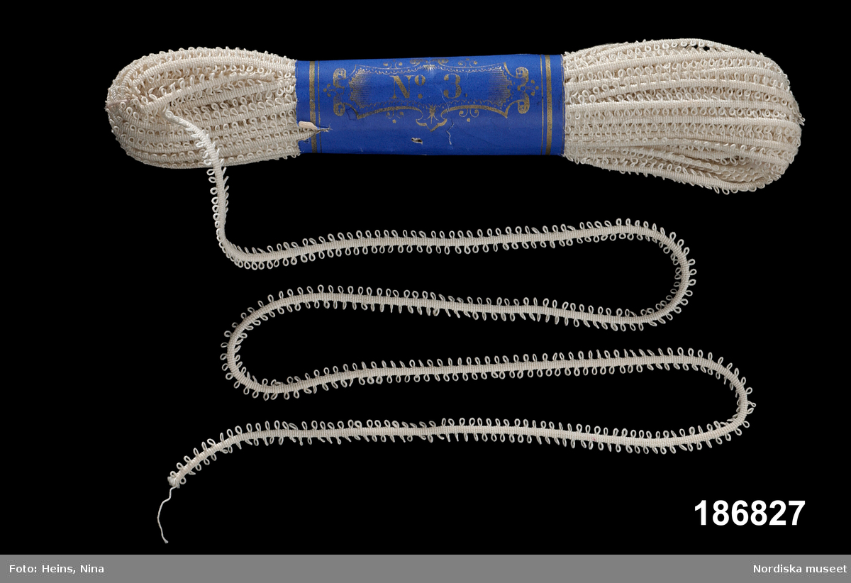Spetsband.
Linne.
Maskingjort rundvävt smalt band med två jämna rader öglor. Metervara som ligger buntat med blå maggördel med "No. 3" i guldtryck.
/Berit Eldvik 2002