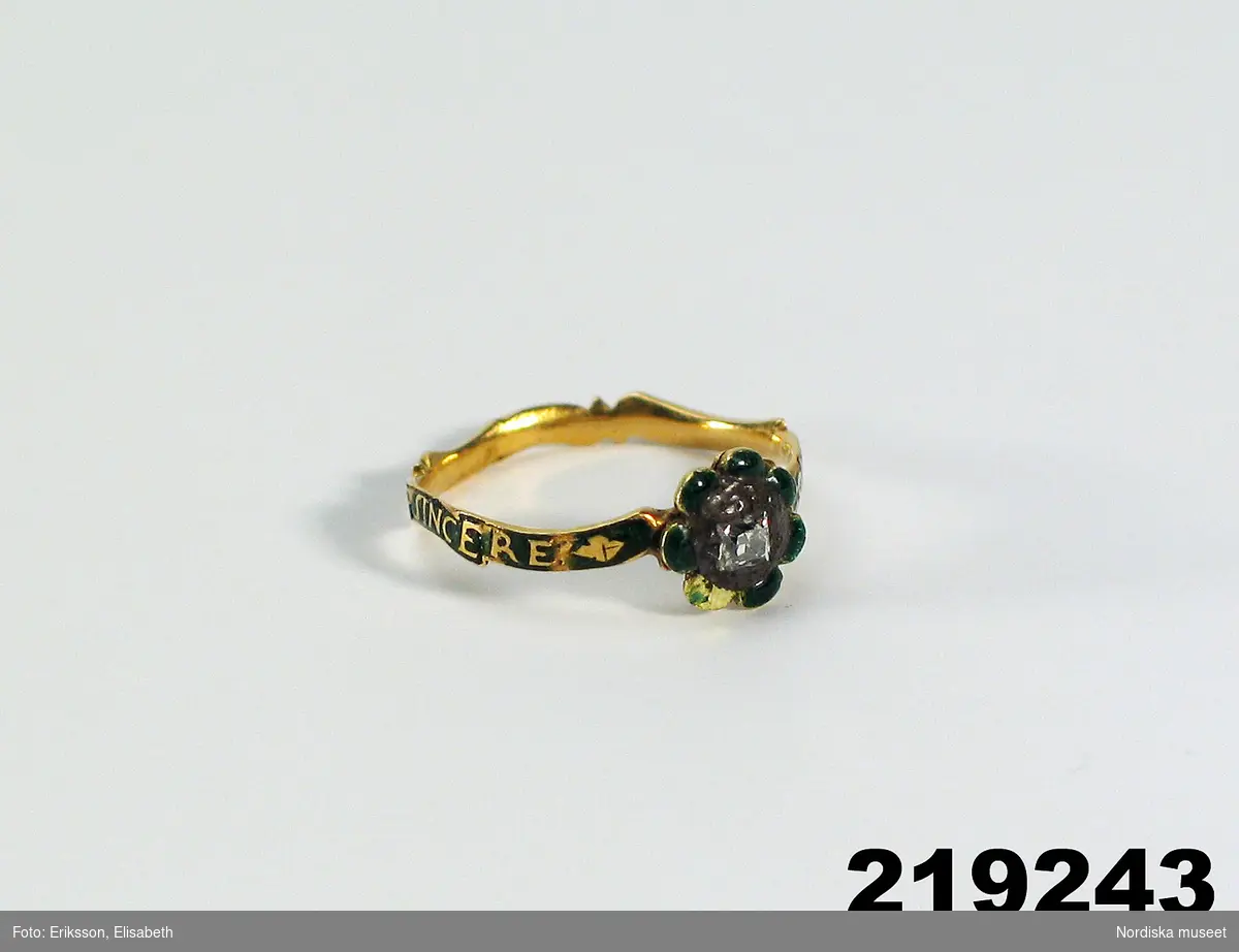 Huvudliggaren (år 1939):
"219243 Fingerring, guld, emaljinläggning; infattad briljant; 'Constante et sincere'; D som 219241 [= 4/4 1933 från Statens Hist. Museum, Stockholm. Jämte 219148ff. Inv.nr 219237-259, 261-280 anträffade år 1900 vid sprängningsarbeten i Stadsgården i Stockholm, 'troligen ett tjuvbyte'.) Statens Hist. Museum 11095:8. Bil." "[Tillskrivet med kulspets:] Emaljen skadad i samband med utställn. 1962. Ändr. av M.P. [= Mona Palmé]"