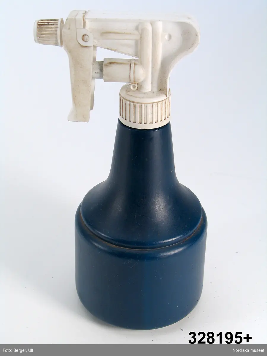 Sprayflaska av formgjuten mörkblå plast, skruvkork med påsittande sprayanordning av vit formgjuten hårdare plast, smalt vattenrör av genomskinlig plast. Under regleraren för vattenstrålen "SPRAYPLAST" i upphöjd text, på sidan rund prägling som visar tillverkningstid: mars 2001. På flaskans undersida etikett med streckkod, därunder "SPRAYFLASKA" m.m.
Anm: Den vita plasten solkig.

Flaskan har använts i samband med dekorering av kista inför begravning.Efter fastsättande av blommor på kistan har dessa sprayats med vatten för att få upp fräschören. Se även unicabox inv.nr 328194 och häftpistol inv.nr 328196.
Elisabeth Brundin 2005-02-29