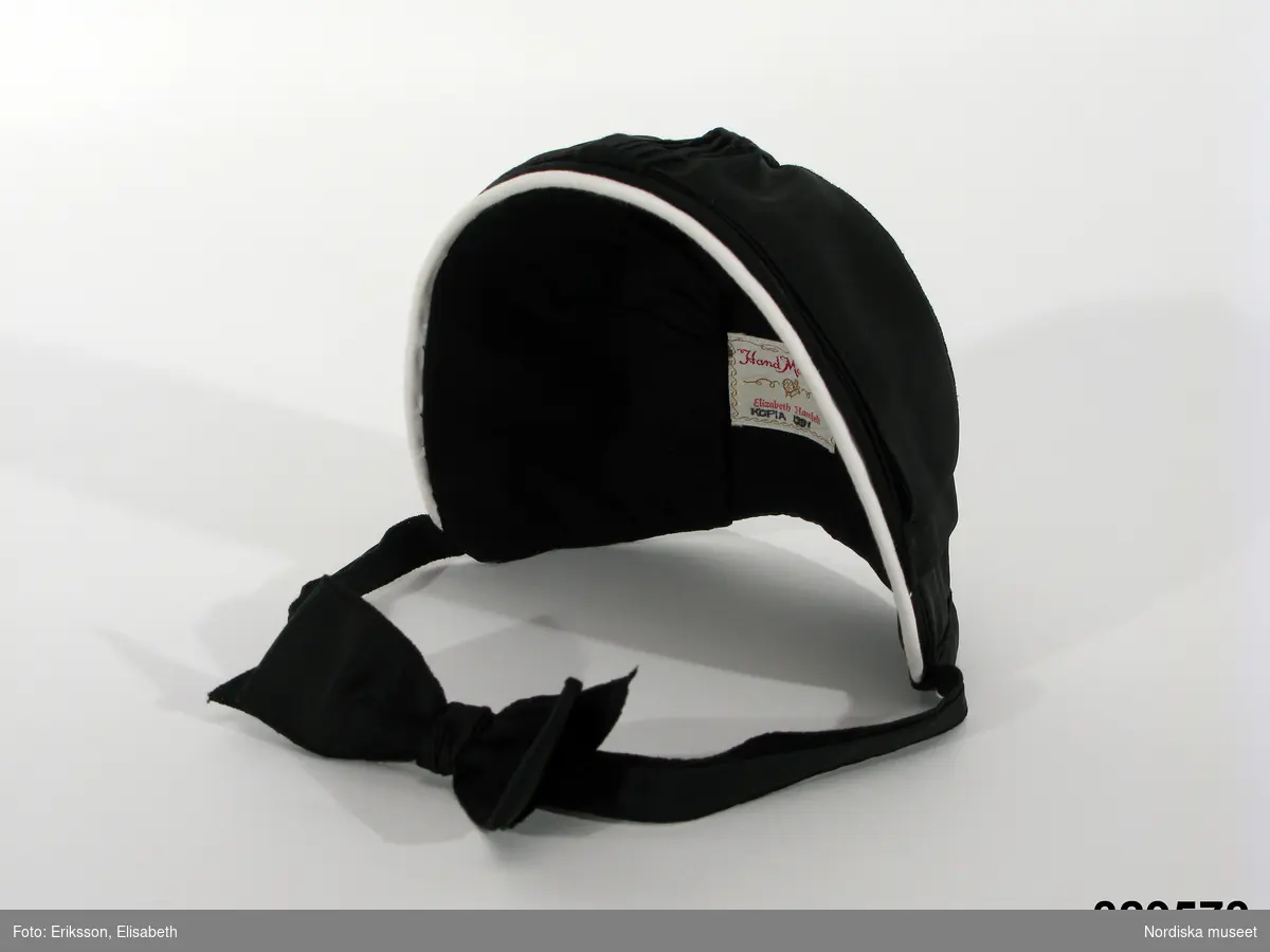 Svart hatt (nackhatt) som ingått i uniform/arbetsdräkt för kvinnlig överkonstapel vid svenska fängelser. Detta är en kopia tillverkad 1991, av äldre typ av hatt. Framkanten kantat med vitt bomullsband.
/Cecilia Hammarlund-Larsson 2009-08-31